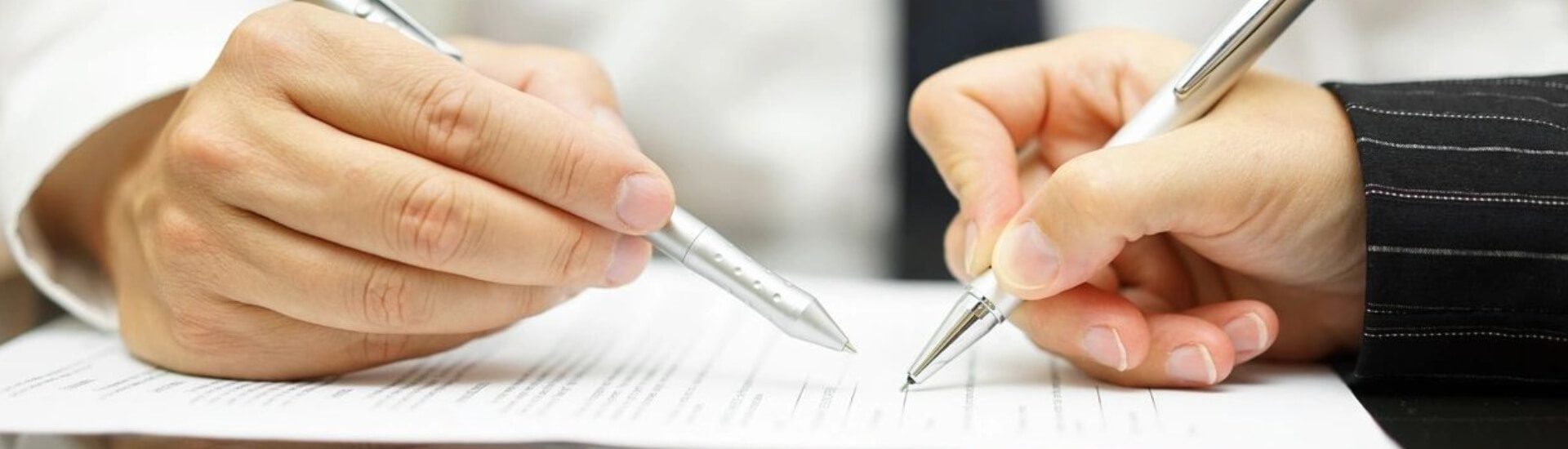 Two people are holding pens and writing on a piece of paper.