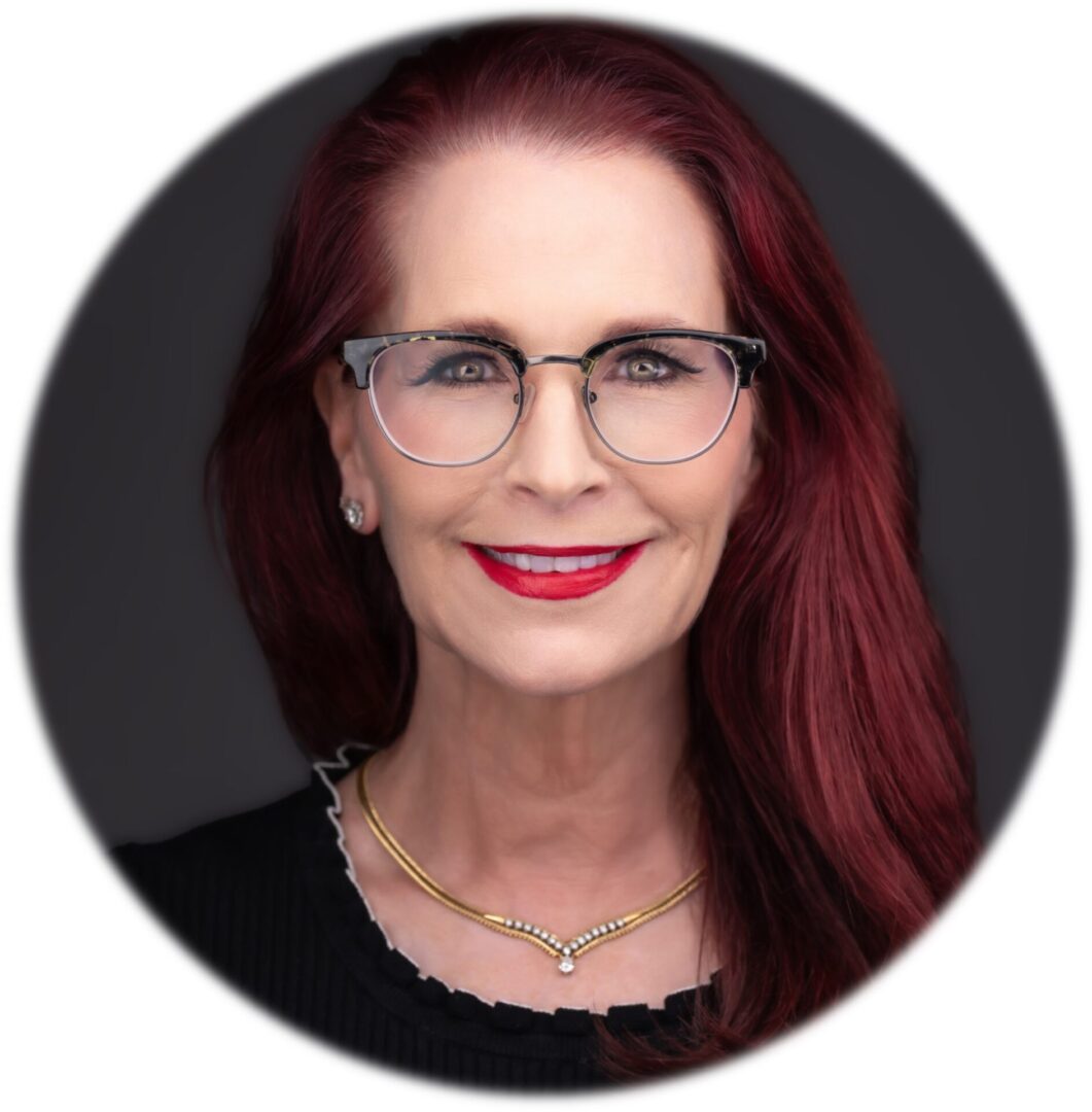 A woman with red hair and glasses is smiling.